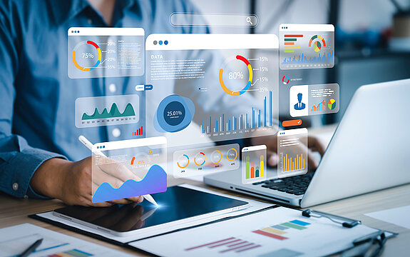 Person arbeitet am Laptop, darüber werden verschiedene Diagramme und Statistiken projeziert